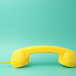 A yellow retro telephone receiver on turquoise blue background.